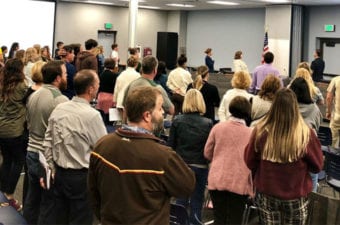 People in board room standing up crossing their hearts for pledge of allegiance
