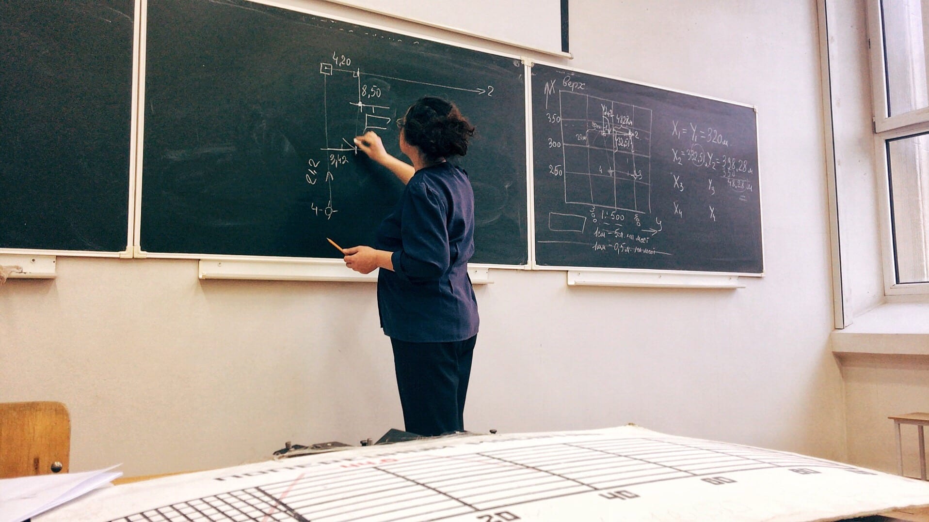 Woman stands at chalkboard and writes a math equation on the board with chalk