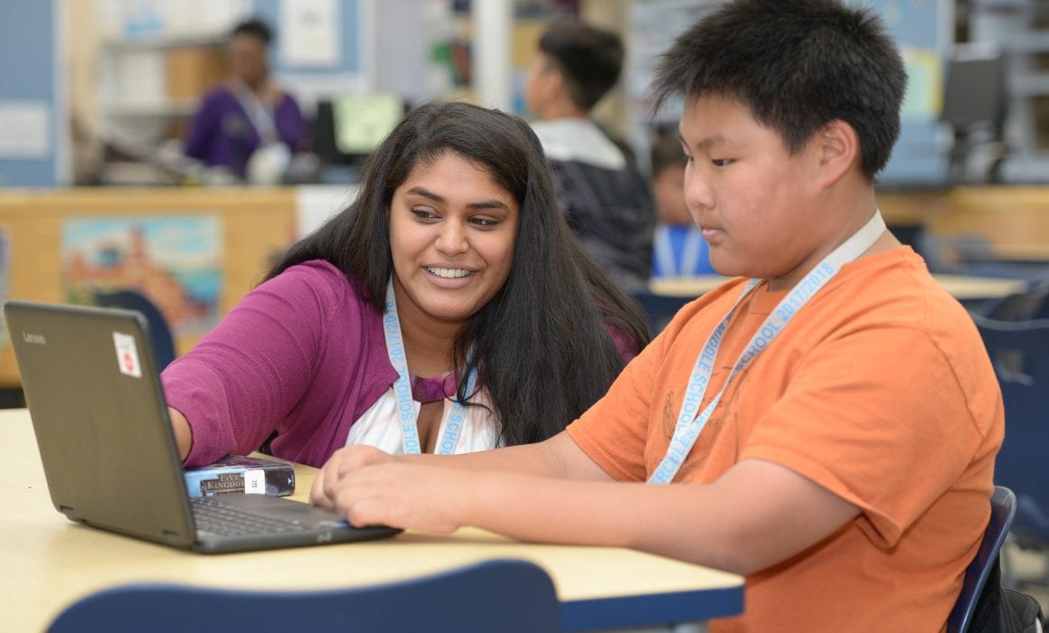 Teacher would with student on laptop