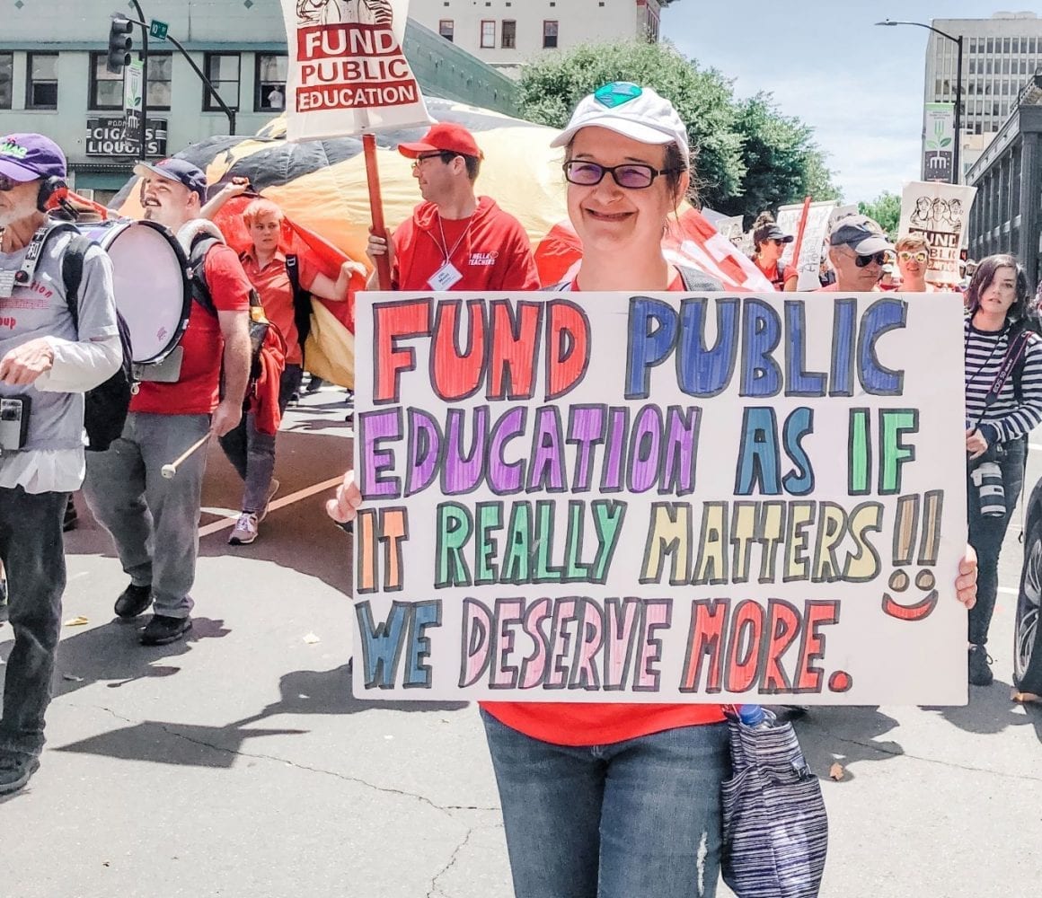 Woman in Red holds sign: Fund Public Education as it if it really matters! We deserve more.