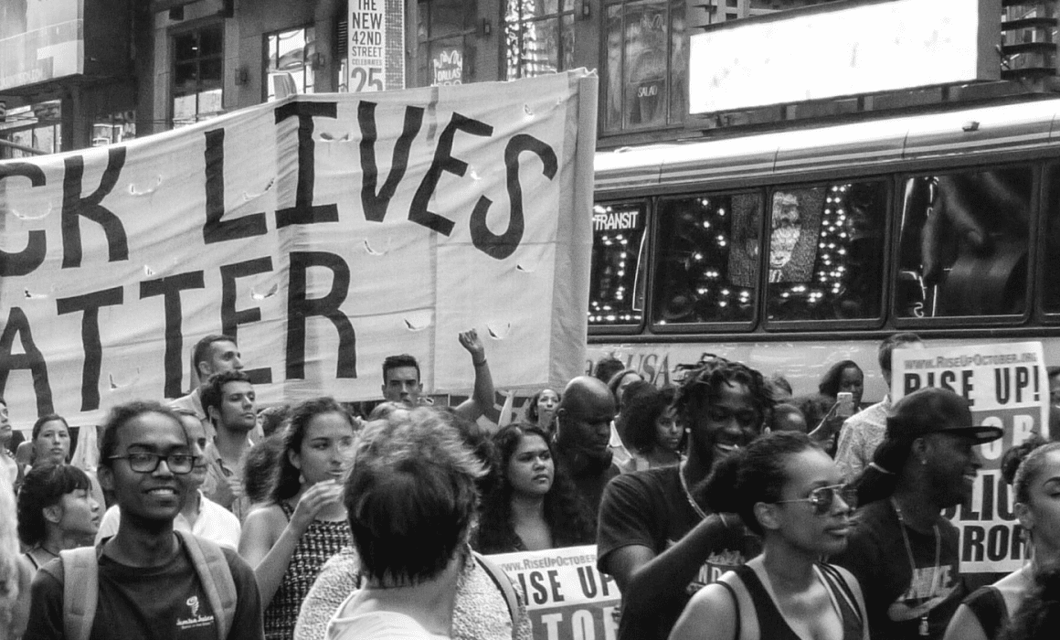 People march together holding a Black Lives Matter sign, image is in black and white.