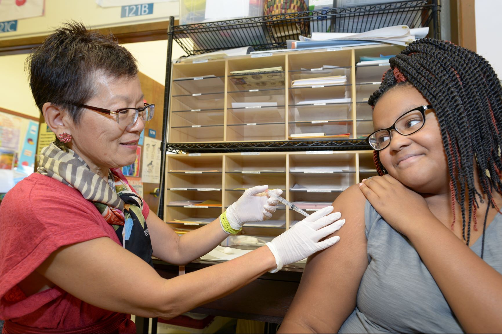 School nurse wearing a pink shirt and scarf gives shot to student