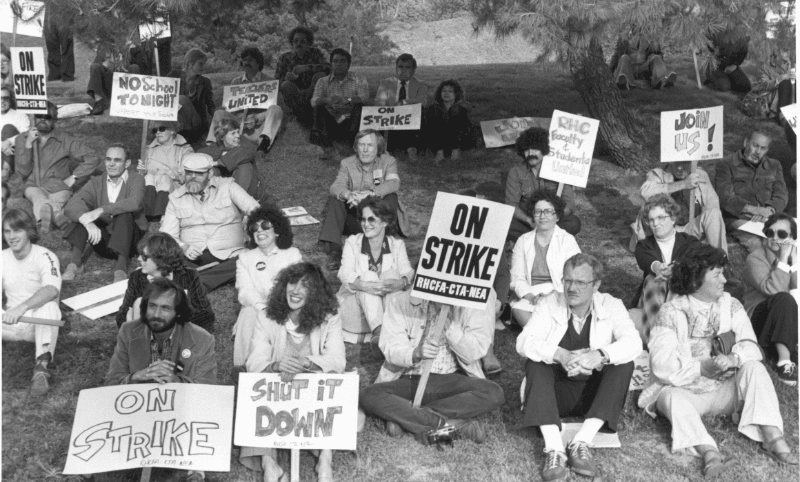 a group of people sit on a lawn with signs that say on strike, shut it down