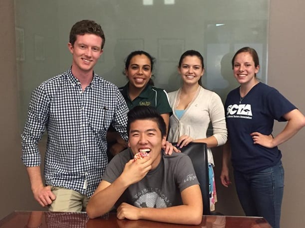 5 students smiling, one eating a donut 