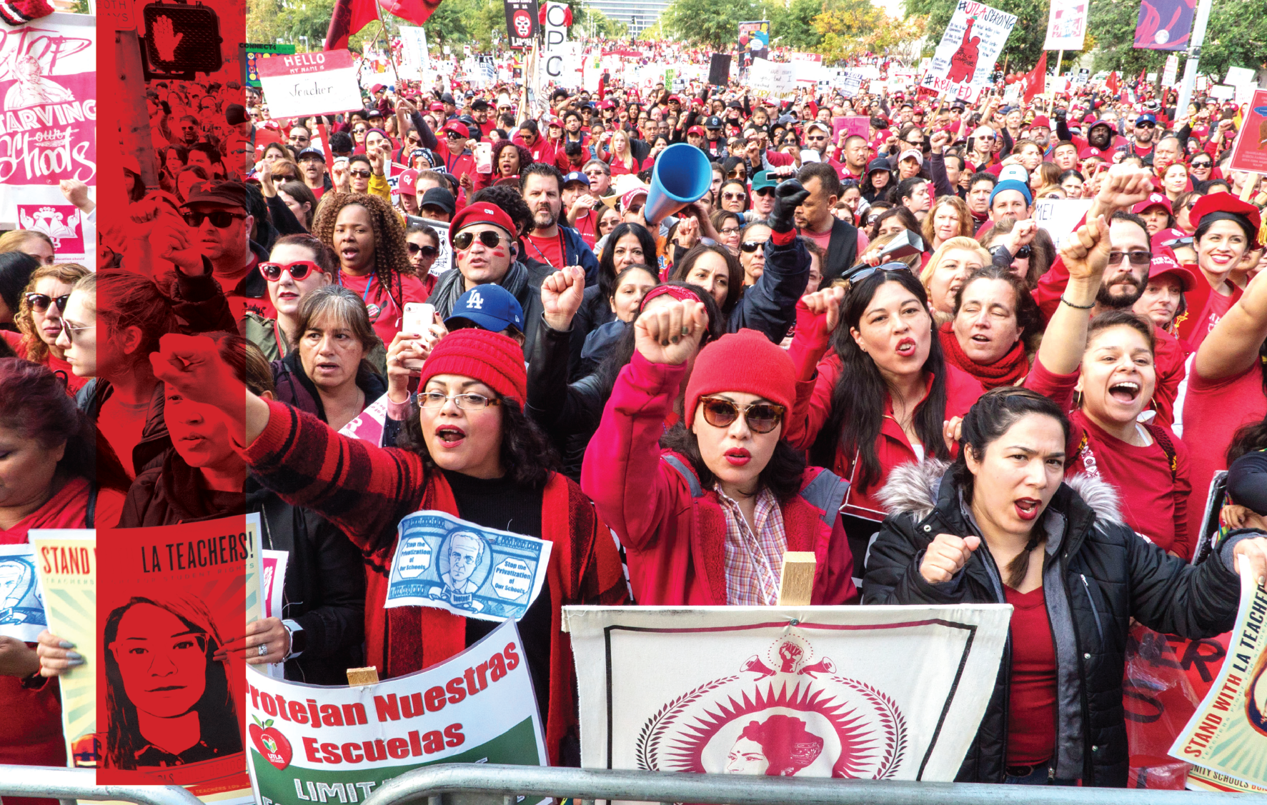 A sea of educators wearing red chants together and hold their firsts in the air, holding signs saying Stand with LA Teachers