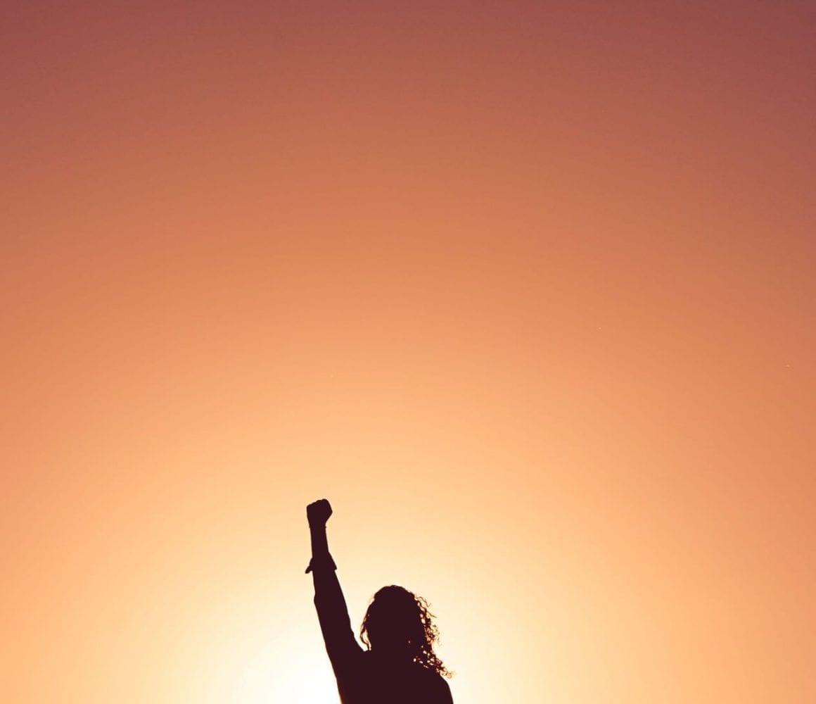 woman stands with fist in the air backlit by the sunset