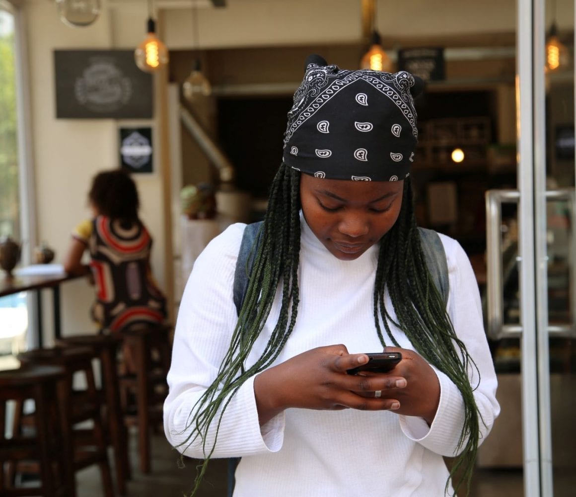 A young woman in a white shirt with a black and white bandana looks down at mobile phone.