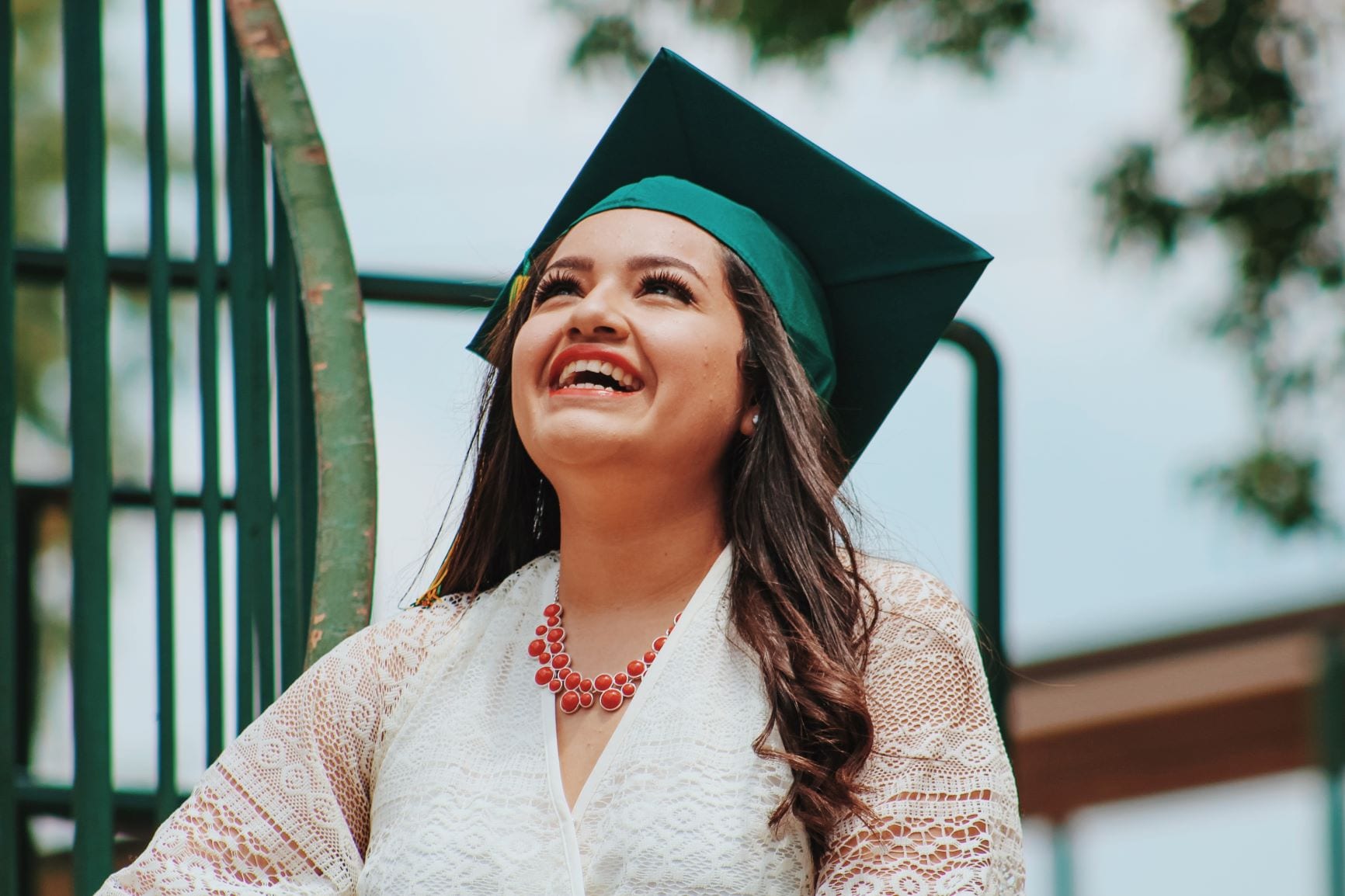 Woman wearing white and graduation cap looks up and smiles