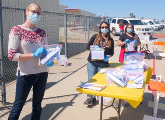 Three teachers in masks handing out packages to help the community