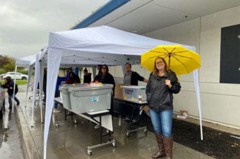 Person standing outside in the rain holding a yellow umbrella near a tent with people under it.