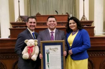 People inside the State Capital holding a bear and recognition plaque smiling