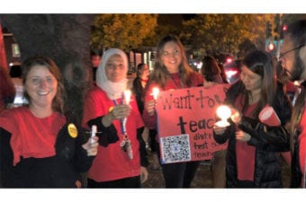 People standing holding up lighted candles smiling all wearing red shirts