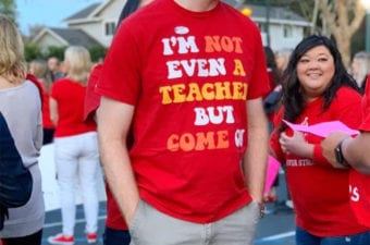 Person standing outside next to lady wearing red shirts that says "I'm not even a teacher but come on."
