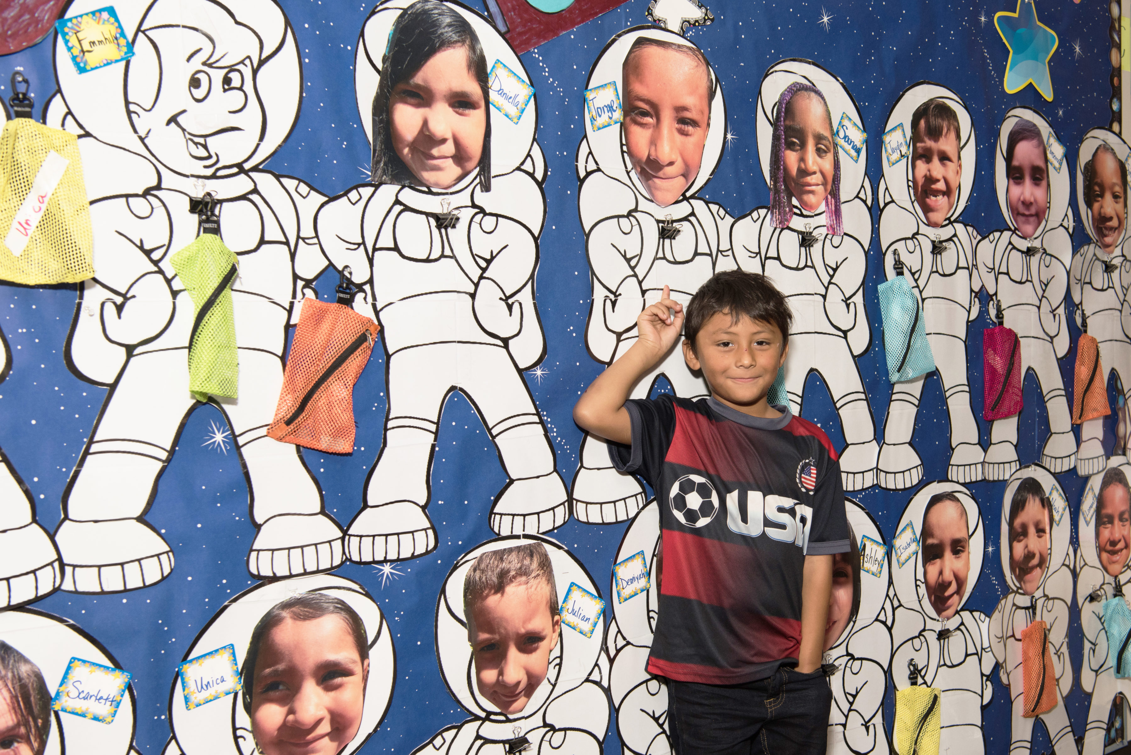 Young boy points to picture of himself as an astronaut on classroom wall.