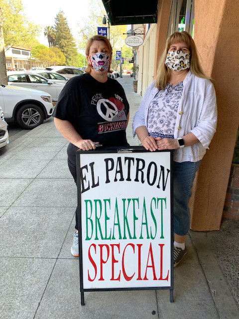 Two women standing on sidewalk by "El Patron" sign