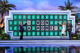Laura Trammell with "Wheel of Fortune" hosts Pat Sajak and Vanna White in front of big board with words: "I won a home!"