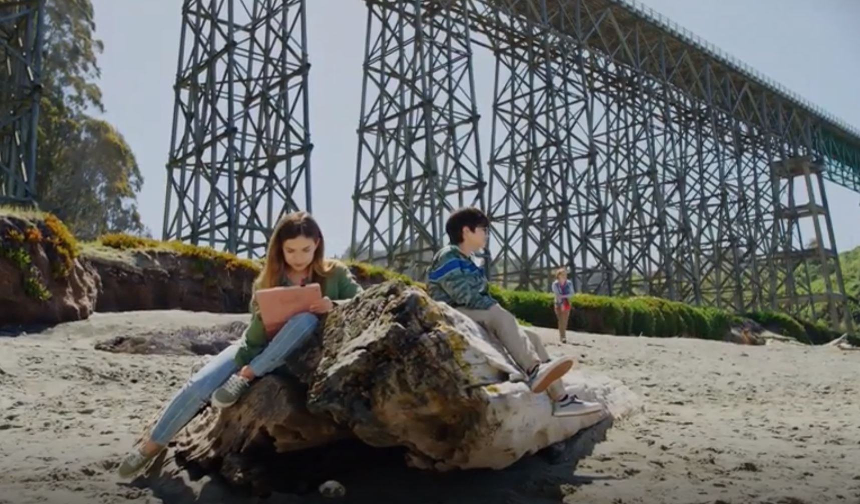 Three kids on beach, trestle bridge in background