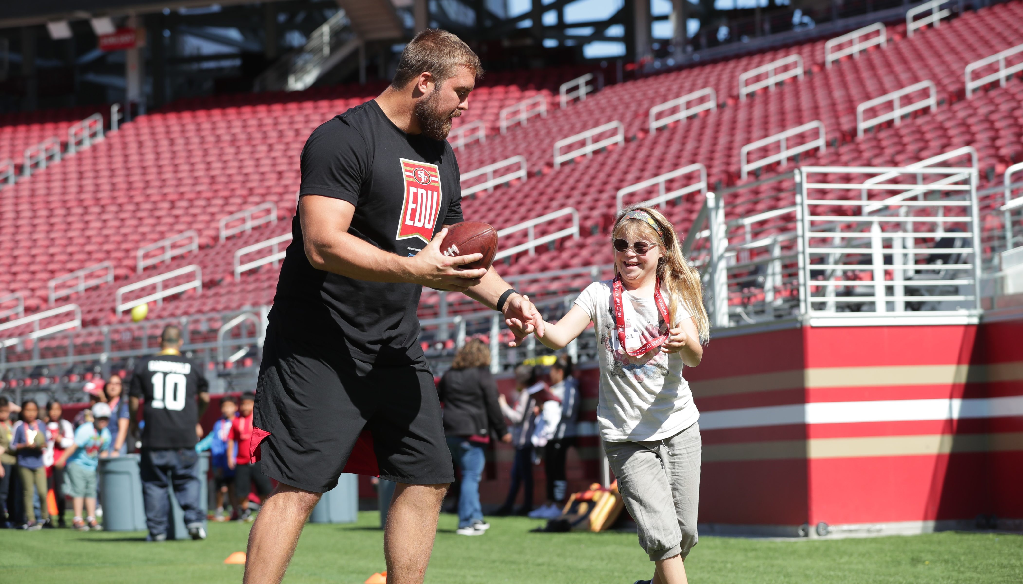 49ers player Robbie Gould with a student on the playing field.