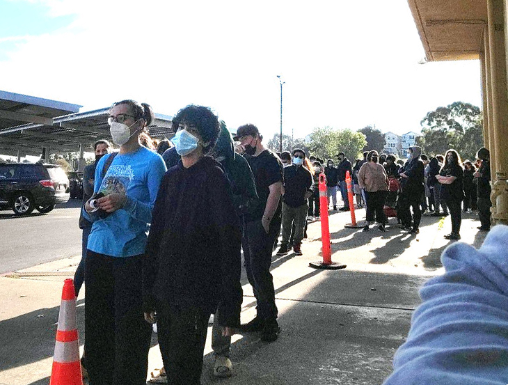 Masked people lined up, waiting for COVID tests