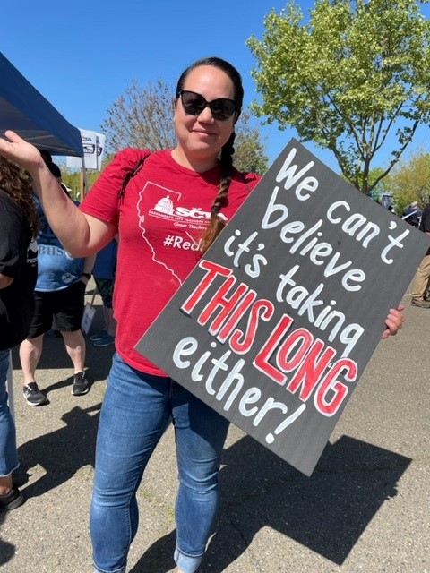 An educator holds a sign that reads we cant believe its taking this long either