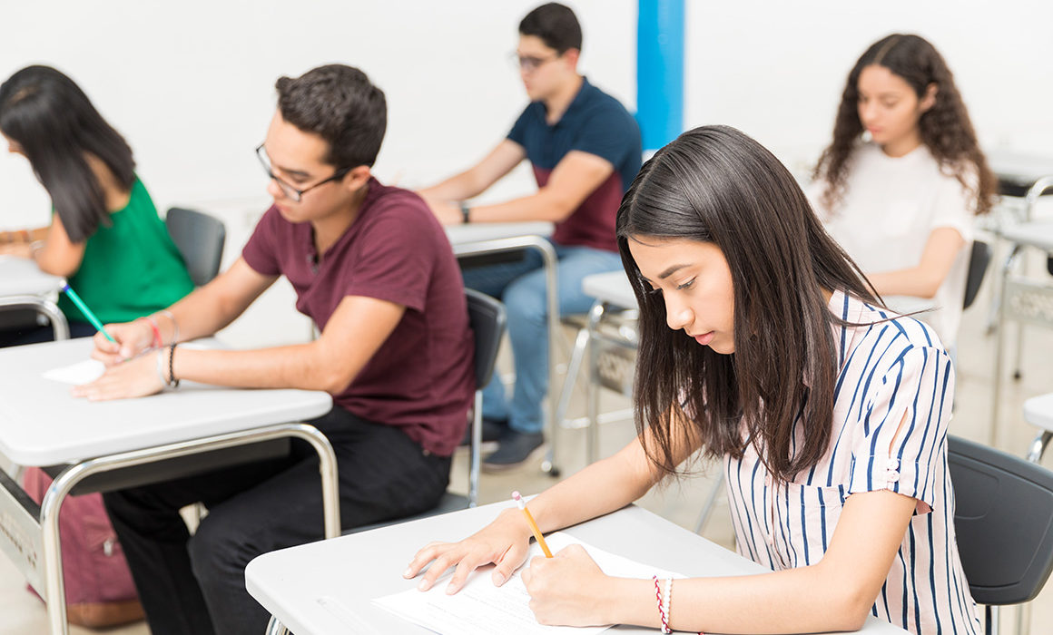 Group of teenage pupils taking test in classroom at university.