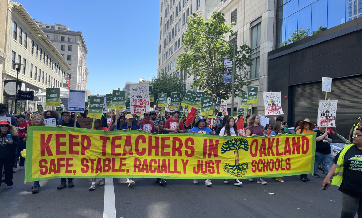 Protestors marching with a big yellow banner with red text