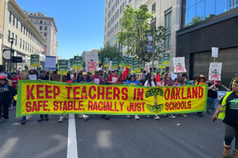 Protestors marching with a big yellow banner with red text