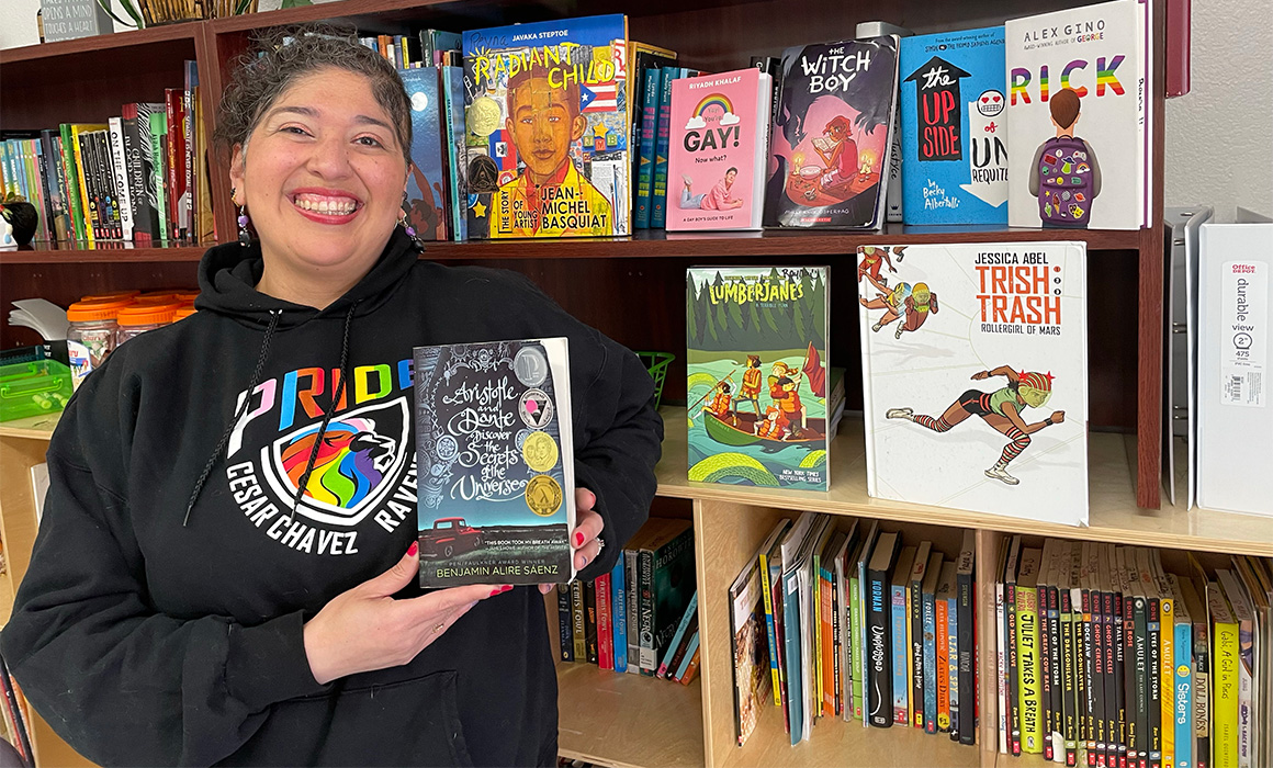 Image of a teacher holding up a book while standing in front of a library of books.