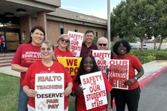Seven educators stand in front of a building titled Rialto Unified School district holding picket signs that read Rialto Teachers Deserve Fair Pay and Safety for Our Students and Staff.