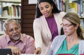 Photo of three professional adults talking at a desk