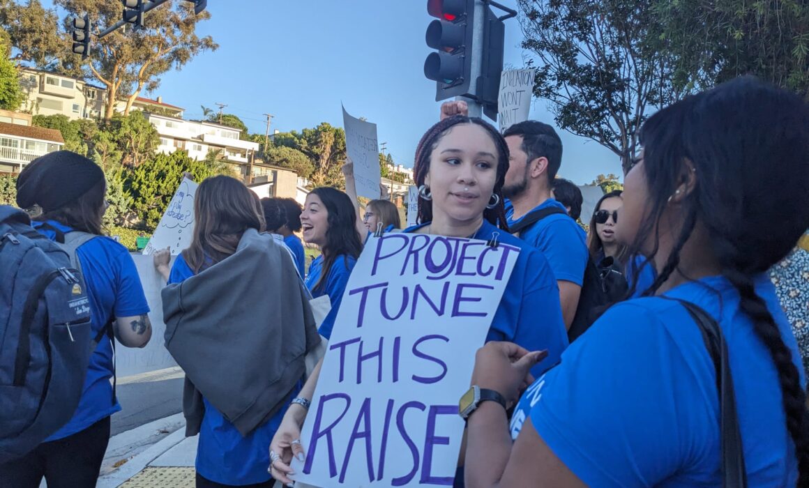 A group of people standing together in blue shirts with one holding a sign that reads "Project Tune This Raise."