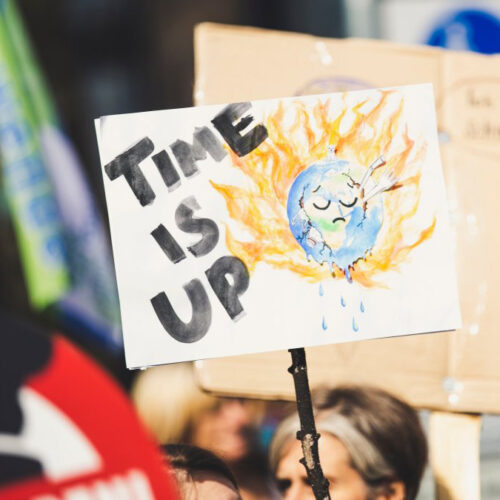 Image of a protest sign with the words "Time Is Up" and a drawing of a burning sun.
