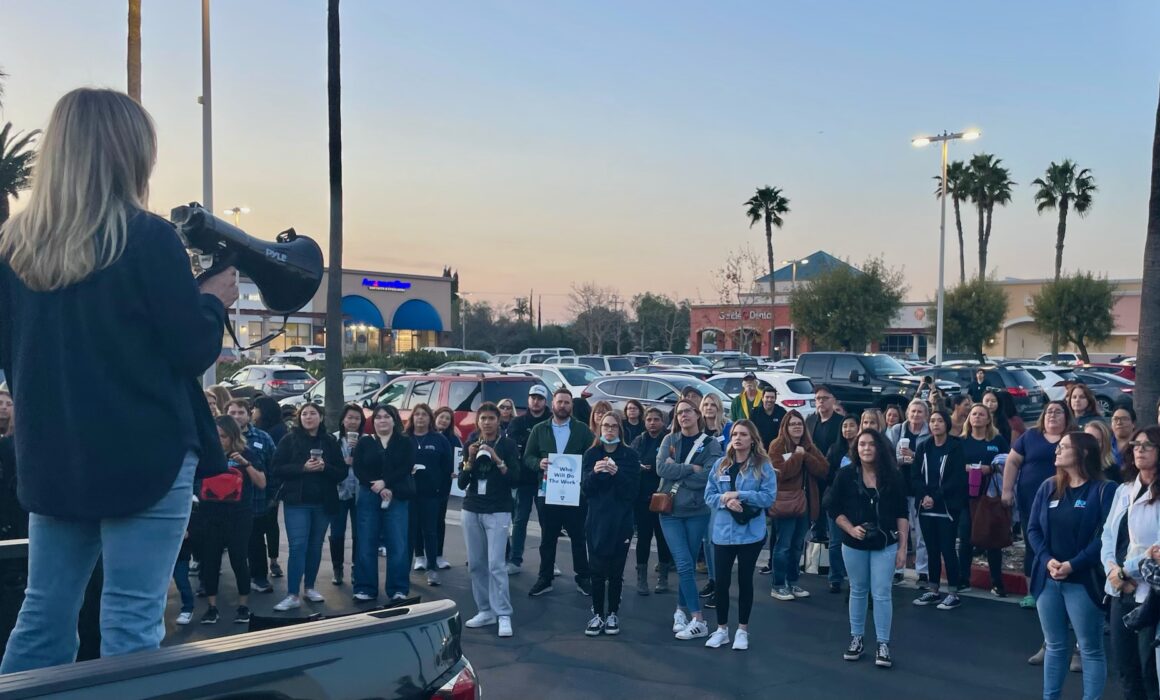 A person holding a bullhorn stands on a pickup truck while a crowd of people watches.