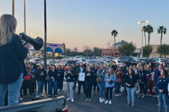 A person holding a bullhorn stands on a pickup truck while a crowd of people watches.