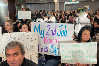 A crowd of people holding up signs that with messages of support for teachers and students.