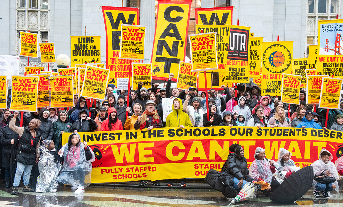 A crowd of people holding We Can't Wait picket signs pose for a photo.